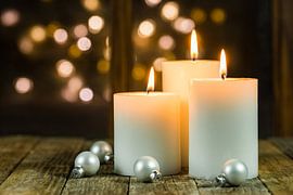 Christmas or Advent candles on wooden table in front of window lights background by Alex Winter