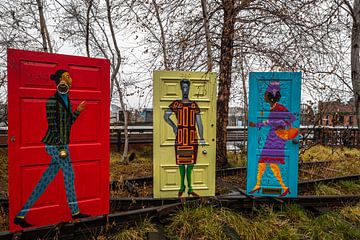 Schilderij van Afro-Amerikaanse mannen- en vrouwenfiguren op rode, gele en blauwe deuren in openluch van Mohamed Abdelrazek