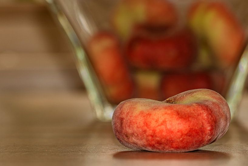 A flat peach in front of a bowl of other fruit by Photoart-Naegele