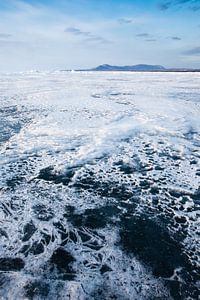 Dunne sneeuw vormt grillige patronen op het ijs van Baikal en bergen in de verte met de lucht van Michael Semenov
