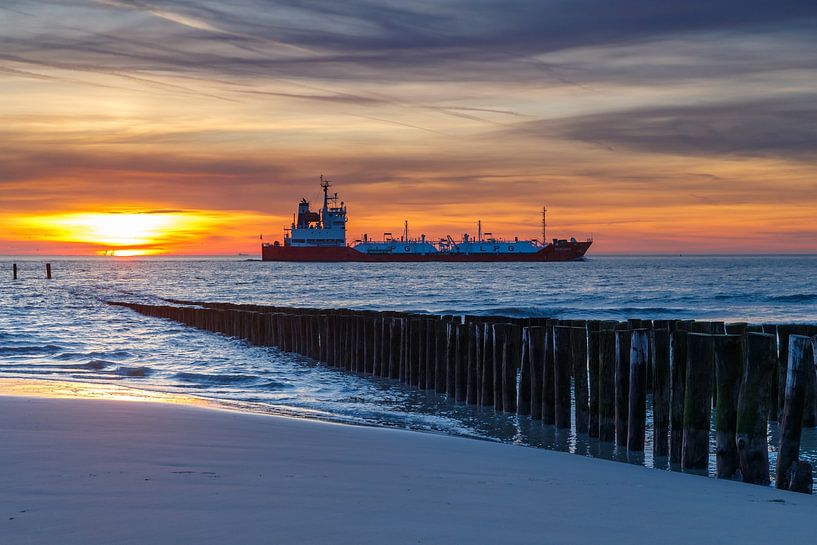 Vrachtschip vaart voorbij aan de kust van Zeeland tijdens zonsondergang. van Menno Schaefer