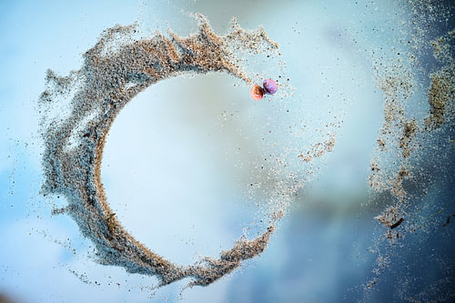 Offener Ring mit Meersand und einer rosa Muschelschale auf blauem Grund