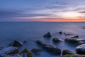 Lange Belichtungszeit, ruhiges Wasser und felsiges Ufer bei Sonnenaufgang am Markermeer in der Nähe von Edam, Niederlande