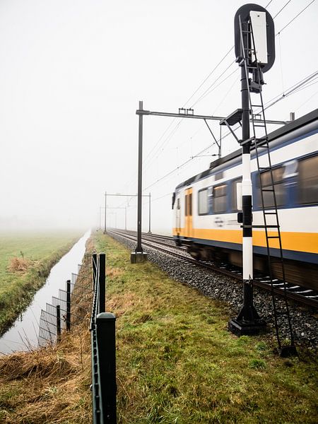 Un train typiquement hollandais sort du brouillard et passe un signal de chemin de fer par Hans Post