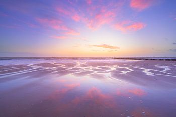 Le ciel rouge du soir se reflète sur le sable mouillé de la plage.