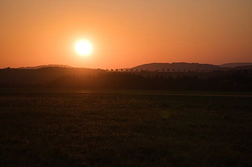Romantischer Sonnenuntergang hinter einem Hügel vor einer Wiese.