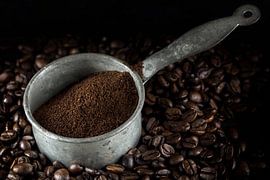 kleine Metallkanne mit gemahlenem Kaffee auf einem Haufen ganzer gerösteter Kaffeebohnen, dunkler Hi von Maren Winter