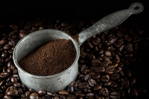 kleine Metallkanne mit gemahlenem Kaffee auf einem Haufen ganzer gerösteter Kaffeebohnen, dunkler Hi