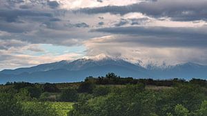 Zonverlichte, besneeuwde top van de Franse Pyreneeën onder een dreigende wolkenlucht. van Haarms