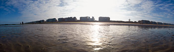 Vues panoramiques d'une plage de sable avec un horizon urbain et un ciel ensoleillé.