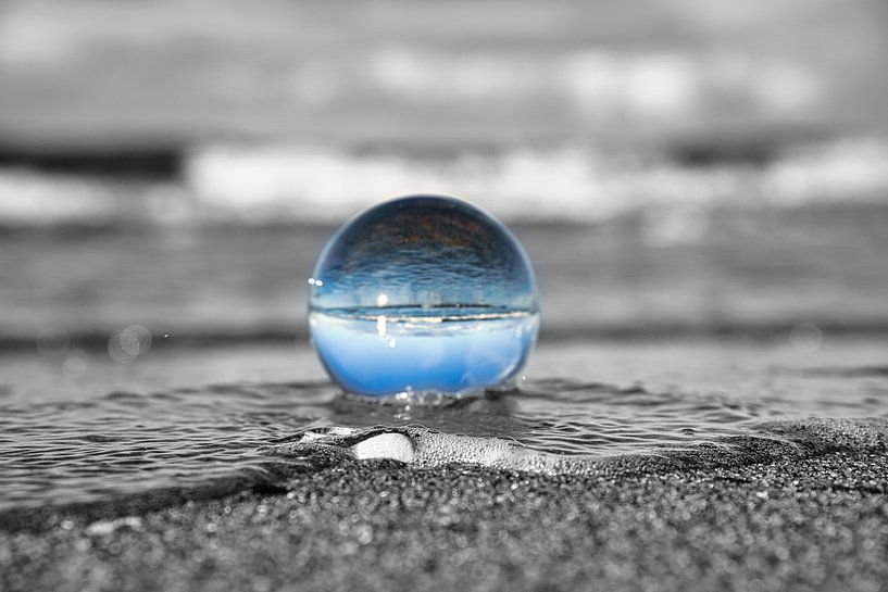 Glass ball on the beach of the Baltic Sea. Black and white photo with a colored glass ball in which  by Martin Köbsch