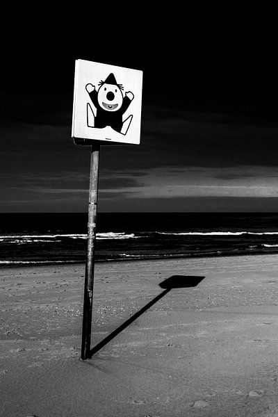 Zwart-wit foto van een bord met een clown op het strand van Wim Stolwerk