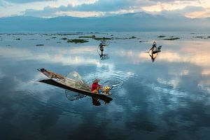 Visser die met traditionele boot op het Inle meer in Myanmar op ouderwetse wijze met een vis korf vi