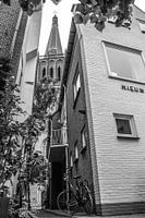 Black and white photo of an old narrow alley with a bicycle in the alley and a view of a church towe