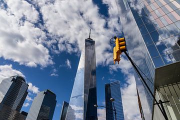 Reflectie blauwe lucht en wolken in de ramen van de hoogbouw met geel verkeerslicht in New York. van John Duurkoop