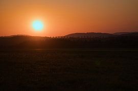 Coucher de soleil romantique derrière une colline devant une prairie.