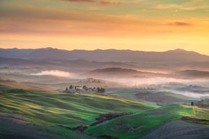 Ein nebliger, goldfarbener Sonnenuntergang über den sanften Hügeln von Volterra