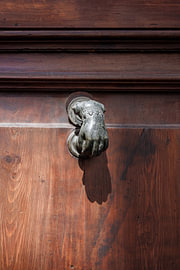 Close-up of a hand-shaped door knocker on a dark wooden door by Christoph Hermann