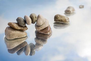 Bogen aus balancierten Kieselsteinen und Trittsteinen im Wasser mit Reflexion, hellblauer Himmel mit von Maren Winter