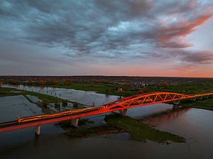 Eisenbahnbrücke in einem farbenprächtigen Sonnenuntergang über dem Fluss IJssel