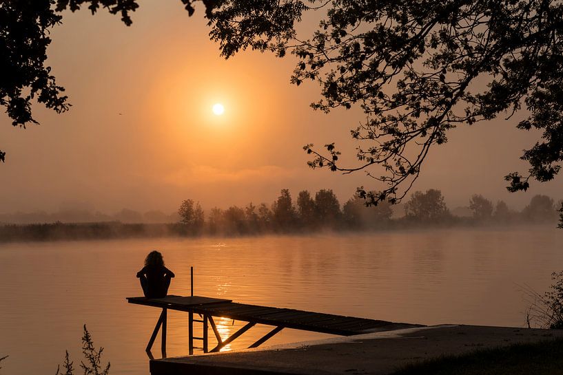 silhouette girl at wooden jetty during sunset in the early morning over the river maas in limburg in by ChrisWillemsen