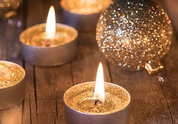 Festlich brennende goldene Advents- und Weihnachtskerzen mit glitzernden Kugeln als Dekoration von Alex Winter