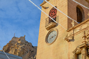 Artistic clock tower of the Basilica of St Mary of Alicante. In the background the Castillo de Santa