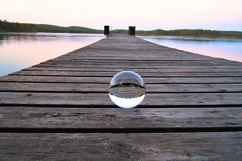 Glass ball on a footbridge reaching into a lake by Martin Köbsch