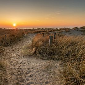 Zandpad door de duinen bij Petten leidend naar de ondergaande zon in de Noordzee van Bram Lubbers