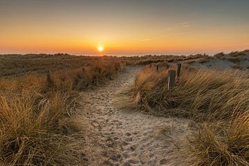 Zandpad door de duinen bij Petten leidend naar de ondergaande zon in de Noordzee van Bram Lubbers