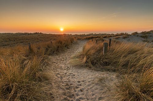 Zandpad door de duinen bij Petten leidend naar de ondergaande zon in de Noordzee