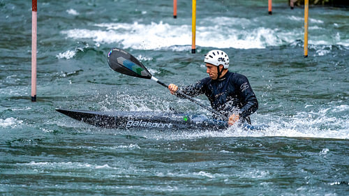 Male athlete competing in white water kayak slalom navigation on