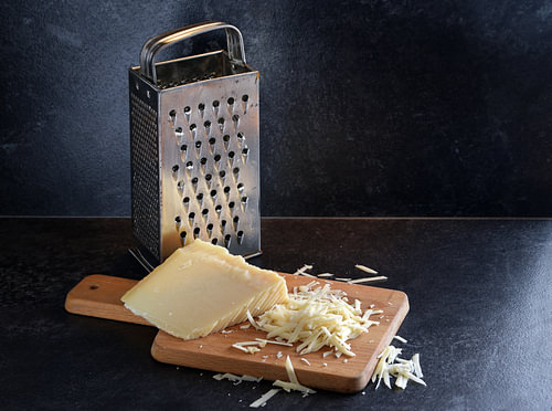 Parmesankäse am Stück und gerieben und eine gebrauchte Metallreibe auf einem hölzernen Schneidebrett