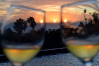 Proostende wijnglazen met zonsondergang boven de zee en zwembad