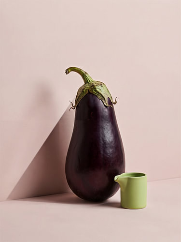 A minimalist still life featuring an aubergine and a green jug