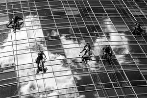 Glazenwassers hangen aan touw terwijl ze de ramen van een glazen wolkenkrabber in Buenos Aires schoo van Wout Kok