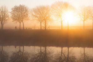 Fietser langs de rivier Leie tijdens een mistige ochtend in de winter met prachtige zonsopkomst in M