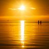 Ein sommerlicher Sonnenuntergang mit zwei Menschen im Wasser von Bas Meelker