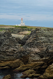 A lighthouse on a rugged coastline: a white building with a red roof next to jagged rocks