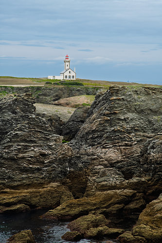 A lighthouse on a rugged coastline: a white building with a red roof next to jagged rocks