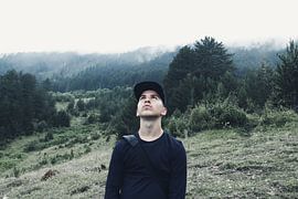 Young hiker stands in the rain and looks up to the cloudy sky by Besa Art
