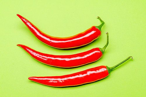 Drie rode chilipepers op een groene ondergrond