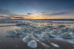 Meeresschaum wird bei einem farbenprächtigen Sonnenuntergang am Strand von Den Helder in der Nähe eines Piers angespült