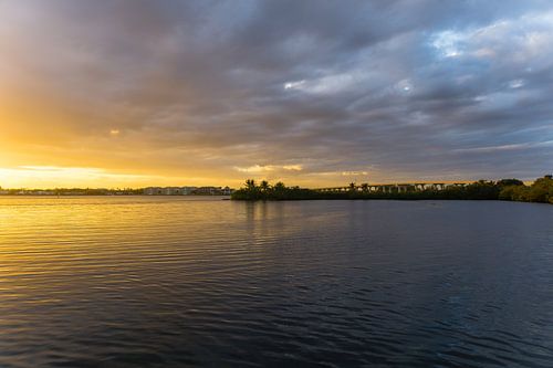 Verenigde Staten, Florida, Oranje gloeiende lucht met enkele wolken en snelwegbrug achter weerspiegelend water