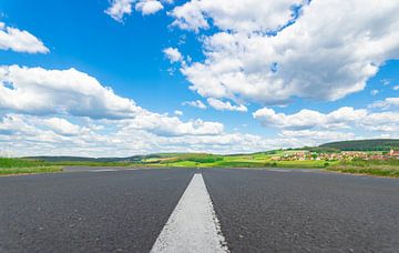 Asphalt road with white dividing lines, beautiful landscape and cloudy blue sunny sky by Alex Winter