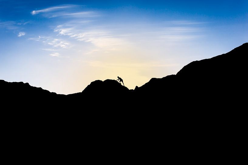 Silhouette van man die berg beklimt bij ondergaande zon. Wout Kok One2expose van Wout Kok