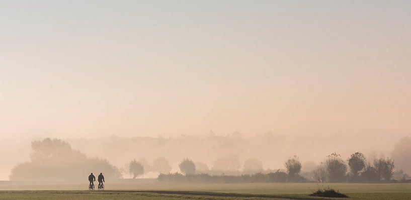 Cyclistes dans les prairies, dans le brouillard du matin par Daan Kloeg