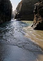 The sun shines through rock formations on the beach