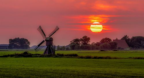 Ondergaande zon met molen friese landschap.