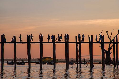 De U Bein brug bij zonsondergang bij zonsondergang met mensen die de Ayeyarwady River oversteken in Mandalay, Myanmar Azië